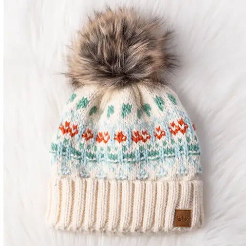 Knitted beanie with floral pattern and fur pom-pom on a white background